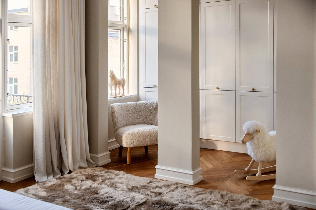 Long-wool sheepskin rug beside the bed in a bright bedroom with tall windows