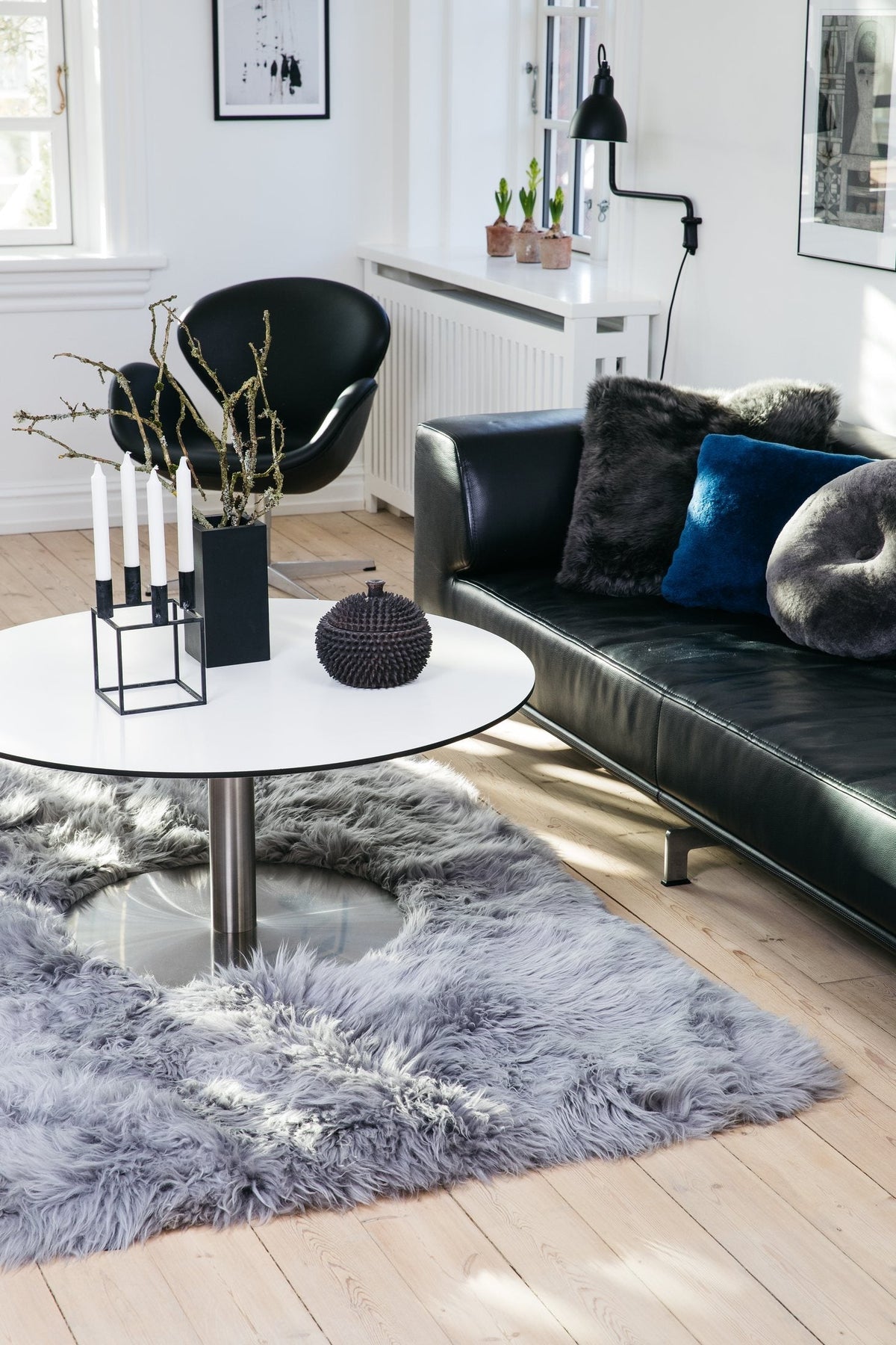 Light gray long-wool sheepskin rug with a cutout around the base of a round table, next to a black leather sofa